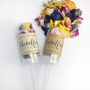 K&ouml;nnte beinhalten: Zwei transparente Plastik-Konfettikanonen zum Hochdr&uuml;cken, gef&uuml;llt mit bunten Bl&uuml;tenbl&auml;ttern. Die Etiketten lauten "Floral confetti, flower petal confetti, eco-friendly, celebration push-pop".