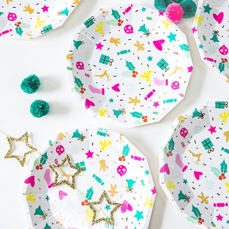 May include: White octagonal paper plates with a festive pattern of gold, pink, teal, and yellow holiday icons. The plates are scattered around teal pom-poms and gold glitter star decorations. A cheerful, colorful design for a holiday celebration.