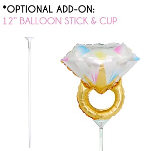 May include: A 12-inch balloon stick and cup, with a clear plastic cup and a white stick. The stick is attached to a gold and clear diamond ring balloon.