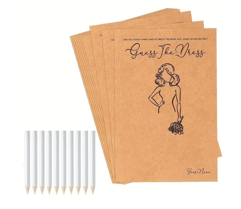 May include: A stack of rectangular tan paper cards featuring the black printed text Guess The Dress, a line drawing of a person holding a bouquet, and the text Your Name, accompanied by ten plain white pencils with unsharpened wooden tips.
