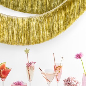 Pu&ograve; includere: Una scena di festa festosa con cocktail rosa, una margarita al melone, popcorn rosa e tartufi al cioccolato. Una ghirlanda di lam&eacute; dorata pende sopra il tavolo, creando un'atmosfera festosa.