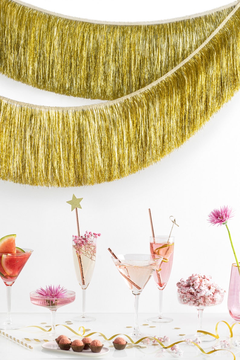 Pu&ograve; includere: Una scena di festa festosa con cocktail rosa, una margarita al melone, popcorn rosa e tartufi al cioccolato. Una ghirlanda di lam&eacute; dorata pende sopra il tavolo, creando un'atmosfera festosa.