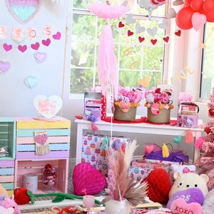 May include: A Valentine's Day party table setting with pink and white decorations. The table is decorated with a pink and white tablecloth, pink and white balloons, and a pink and white unicorn balloon. There are also pink and white heart-shaped decorations and a sign that says "Forever."