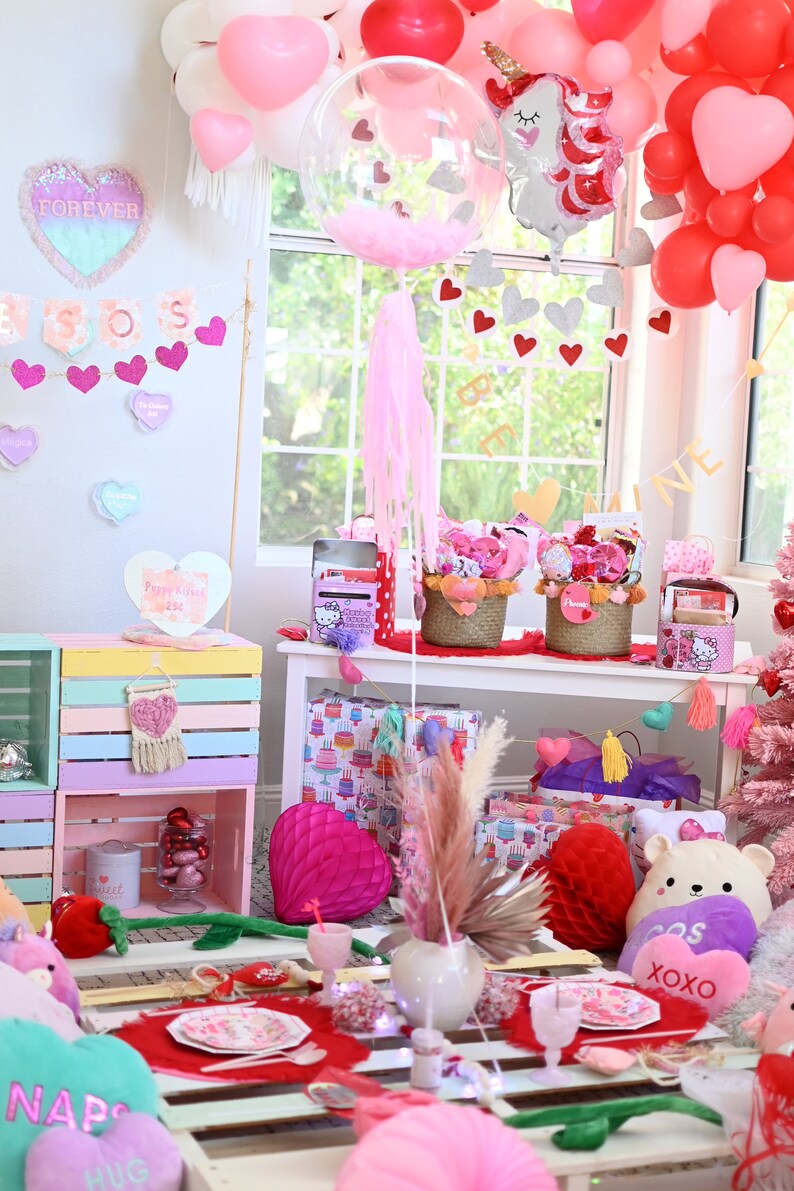 May include: A Valentine's Day party table setting with pink and white decorations. The table is decorated with a pink and white tablecloth, pink and white balloons, and a pink and white unicorn balloon. There are also pink and white heart-shaped decorations and a sign that says "Forever."