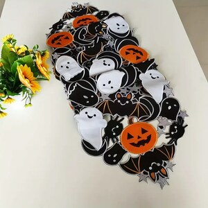 May include: A Halloween-themed table runner featuring black bats, orange jack-o'-lanterns, and white ghosts. The runner is decorated with silver star accents and has a white background. This festive table runner is perfect for Halloween.