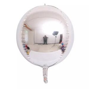 Może przedstawiać: Duży, okrągły, srebrny balon z odblaskową powierzchnią. Balon jest napompowany i ma długi, cienki ogon.