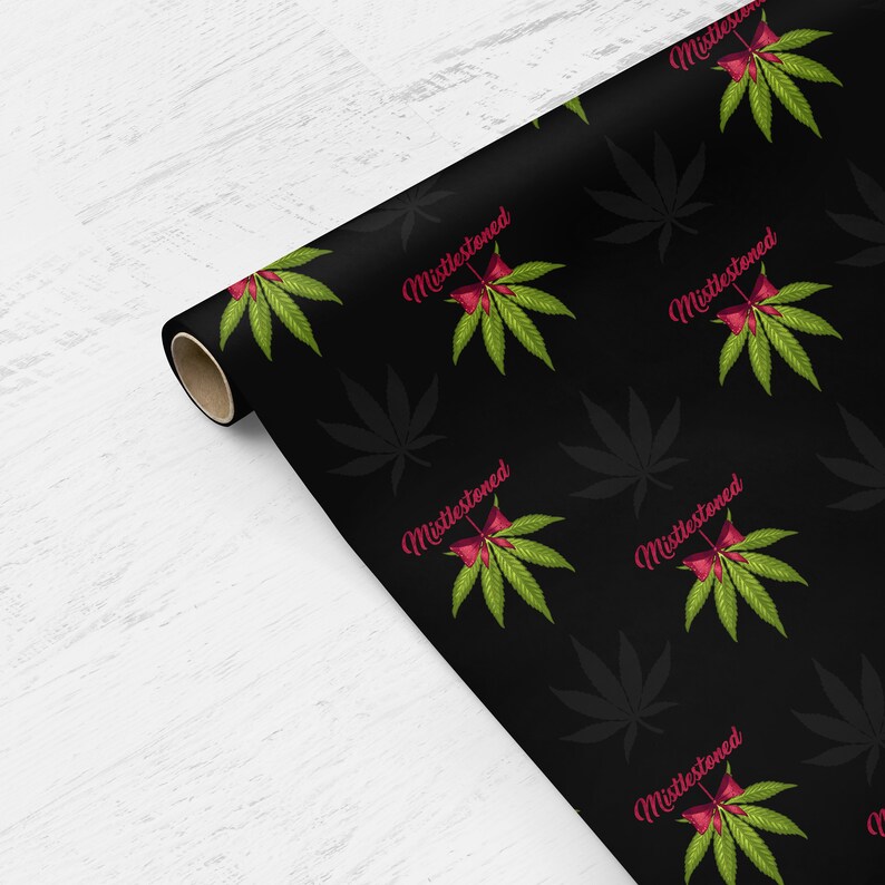 May include: Black wrapping paper with a repeating pattern of green marijuana leaves and red bows with the text "Mistlestoneed" in pink.