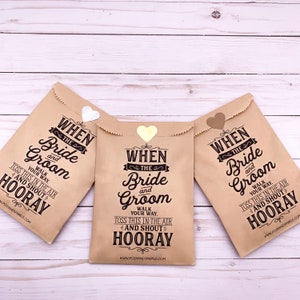 May include: Three brown paper bags with gold heart-shaped stickers. Each bag has the text "When the Bride and Groom" printed on it, with instructions to "Walk your way, toss this in the air and shout Hooray!"