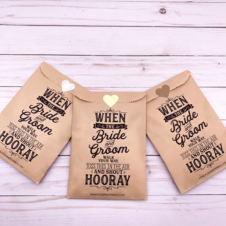 May include: Three brown paper bags with gold heart-shaped stickers. Each bag has the text "When the Bride and Groom" printed on it, with instructions to "Walk your way, toss this in the air and shout Hooray!"