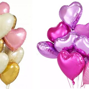 May include: Two bunches of heart-shaped foil balloons. One bunch is pink, gold, and white. The other bunch is purple, pink, and lavender.