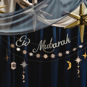 May include: A blue and gold Eid Mubarak banner with stars and crescent moons hanging from a blue curtain. The banner reads "Eid Mubarak" in a white script font.