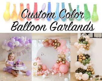 May include: Custom Color Balloon Garlands, a colorful display of balloons in various colors and sizes, including purple, white, pink, gold, green, and cream. The balloons are arranged in a garland shape, creating a festive and celebratory atmosphere.