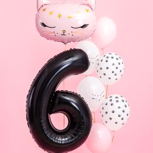 May include: A cluster of birthday balloons in pink, white, and black. The display features a large black number six balloon, a pink cat-shaped balloon, and round balloons with paw prints and star patterns. A festive party decoration.