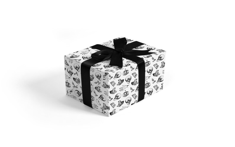 May include: A white gift box with a black ribbon. The box is wrapped in paper with a repeating pattern of black skulls and other spooky designs.