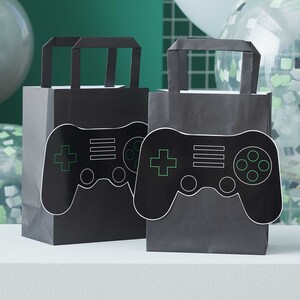 May include: Two black paper gift bags with handles. Each bag has a black and white gamepad design with green accents.