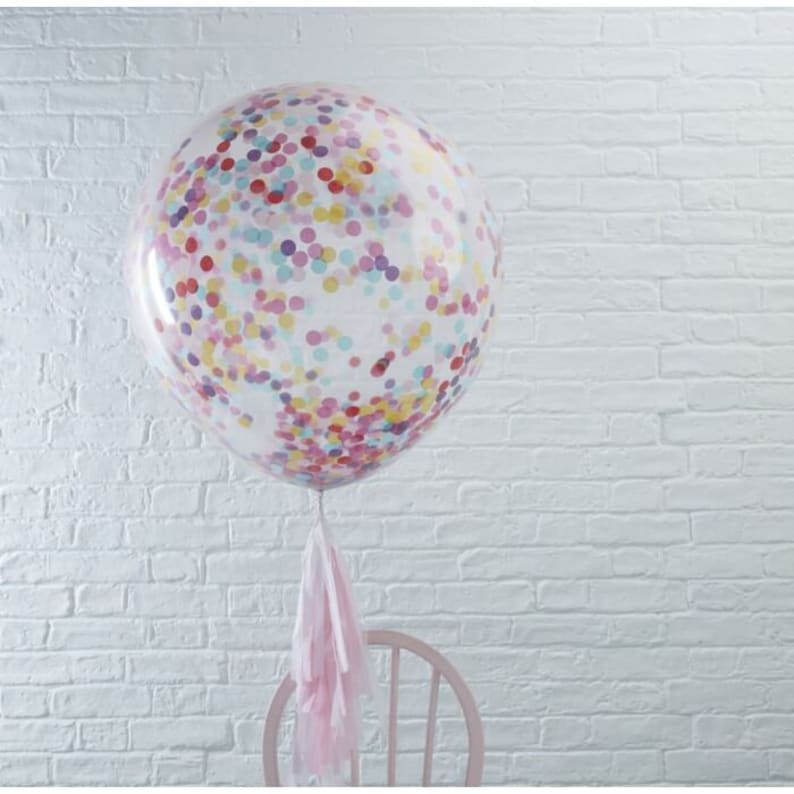 May include: A large, clear balloon filled with colorful confetti. The balloon has a pink tassel attached to the bottom.