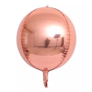 Może przedstawiać: Duży, okrągły balon w kolorze r&oacute;żowego złota z odblaskową powierzchnią. Balon jest napompowany i ma długi, cienki ogon.