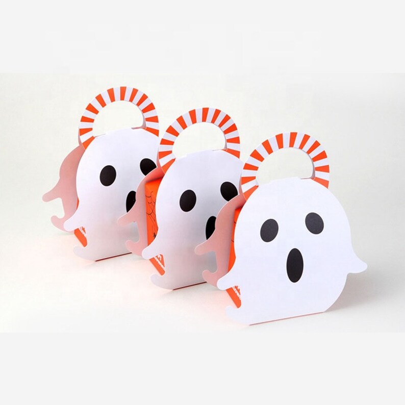 May include: Three white ghost-shaped paper treat boxes with black oval eyes and mouths. Each box features an orange and white striped handle at the top and an orange base with visible black spiderweb graphics on the side panels of the containers.