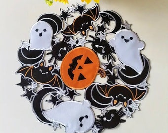 May include: A circular Halloween-themed wall hanging or table centerpiece featuring embroidered fabric patches of white ghosts, black bats, black crescent moons, black stars, and a central orange pumpkin with a black jack-o'-lantern face design.
