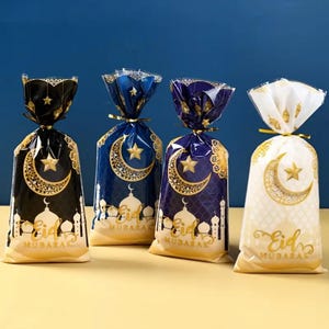 Puede incluir: Cuatro bolsas de regalo de plástico transparente con diseños dorados y azules. Las bolsas presentan una luna creciente, una estrella y una mezquita con el texto "Eid Mubarak".