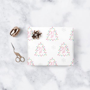 May include: White wrapping paper with a repeating pattern of Christmas lights shaped like a tree with the text "It's Lit" in pink. The paper also has snowflakes.