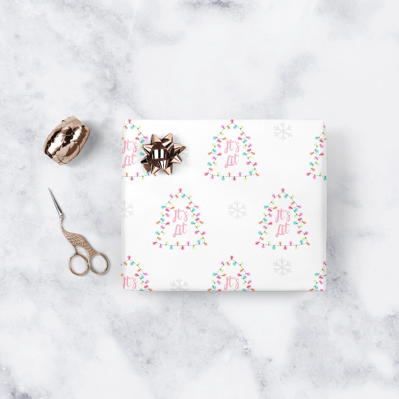 May include: White wrapping paper with a repeating pattern of Christmas lights shaped like a tree with the text "It's Lit" in pink. The paper also has snowflakes.