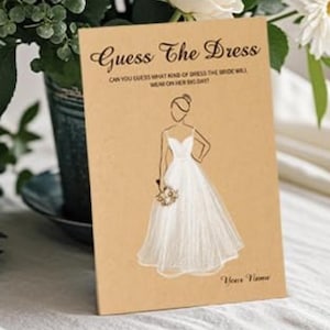 May include: A rectangular tan card featuring the black text Guess The Dress and Can you guess what kind of dress the bride will wear on her big day? with a central line drawing of a person in a white gown holding a bouquet and the text Your Name.
