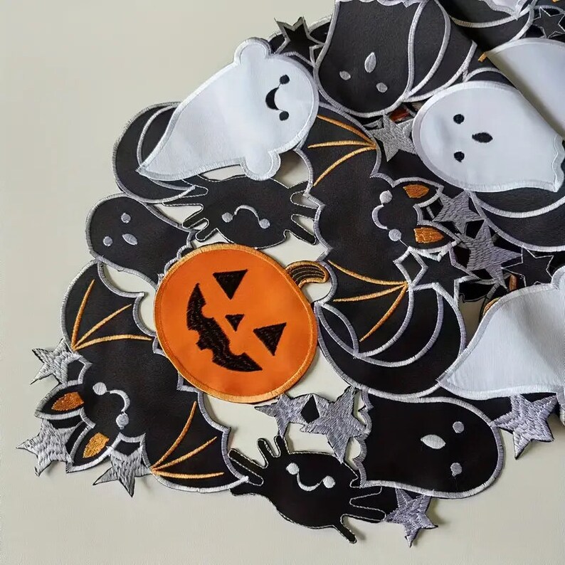 May include: A Halloween-themed table runner featuring embroidered designs of ghosts, bats, spiders, stars, and a jack-o'-lantern. The runner has a white background with black, orange, and silver accents. The design is a festive decoration for the holiday.