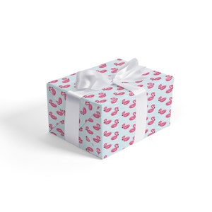 May include: A light blue gift box with a white ribbon. The box is wrapped in paper with a repeating pattern of pink inflatable flamingo pool floats.