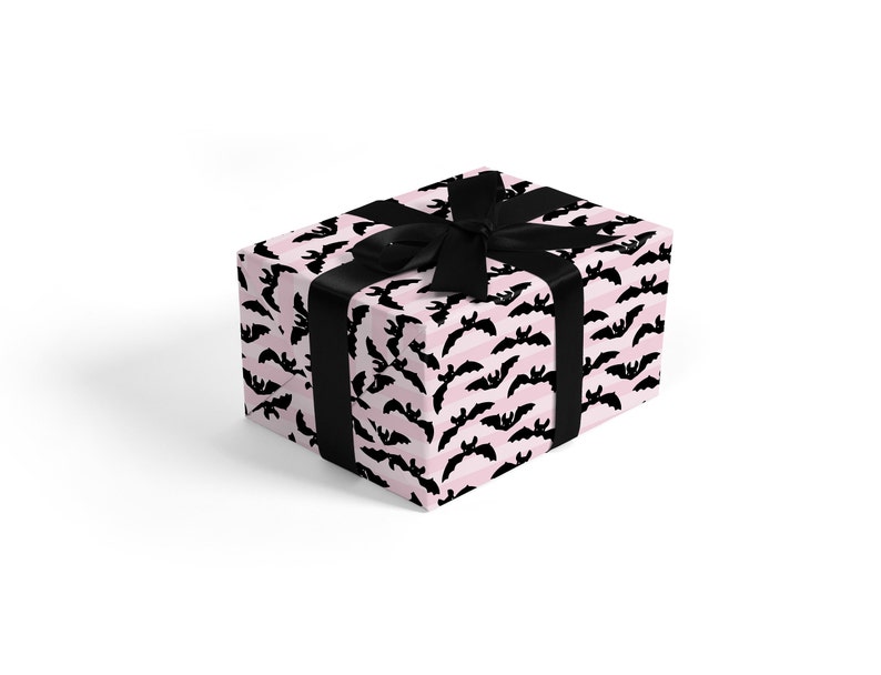 May include: A pink and black gift box with a black ribbon. The box is wrapped in wrapping paper with a pattern of black bats on a pink and white striped background.
