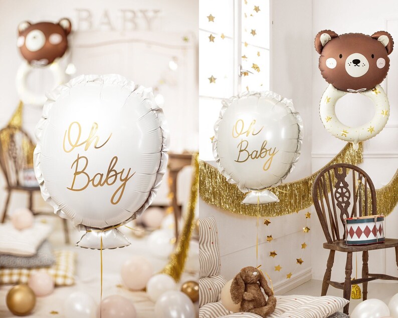 May include: A baby shower decoration set with a white balloon with gold lettering that says "Oh Baby", a brown bear balloon with a gold ring, and gold fringe.