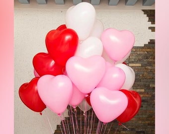 May include: A bouquet of heart-shaped balloons in red, pink, and white. The balloons are clustered together, tied with pink ribbons, and appear to be floating. The background features a textured wall and a light pink border.