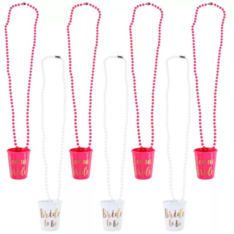 Pu&ograve; includere: Set di sei collane di perline rosa e bianche con bicchieri di plastica attaccati. I bicchieri rosa hanno una scritta dorata che dice "Team Bride". I bicchieri bianchi hanno una scritta dorata che dice "Bride to Be".
