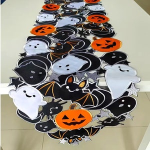 May include: A Halloween-themed table runner featuring a repeating pattern of black bats, orange jack-o'-lanterns, and white ghosts with smiling faces. The runner has a silver trim and star accents, perfect for festive decor.
