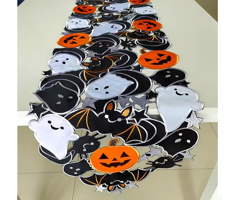 May include: A Halloween-themed table runner featuring a repeating pattern of black bats, orange jack-o'-lanterns, and white ghosts with smiling faces. The runner has a silver trim and star accents, perfect for festive decor.