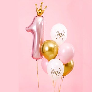 Pu&ograve; includere: Un palloncino rosa a forma di numero uno con una corona dorata in cima, circondato da palloncini dorati, bianchi e rosa con la scritta "One" stampata su di essi.