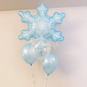 Puede incluir: Un globo azul en forma de copo de nieve con diseños de copos de nieve blancos, rodeado de cuatro globos azules y transparentes con diseños de copos de nieve blancos.