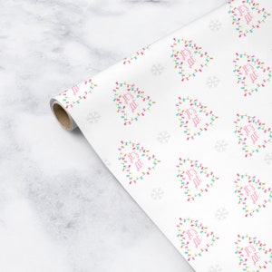 May include: White wrapping paper with a repeating pattern of Christmas trees made of colorful lights. The trees are outlined in white and have the text "It's Lit" in pink letters.