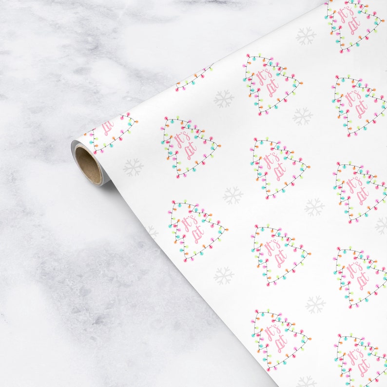 May include: White wrapping paper with a repeating pattern of Christmas trees made of colorful lights. The trees are outlined in white and have the text "It's Lit" in pink letters.