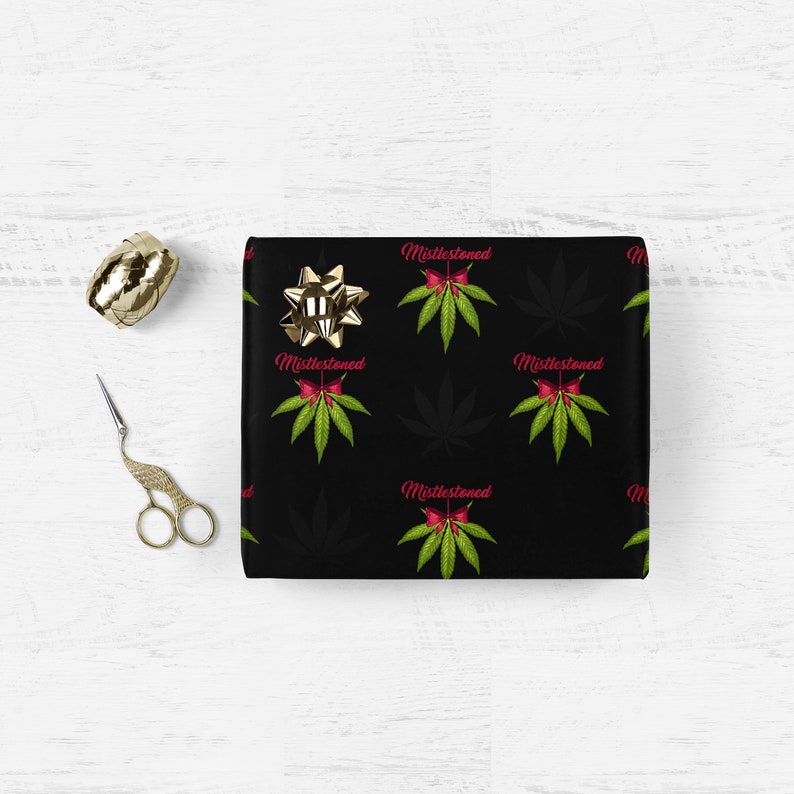 May include: Black wrapping paper with a repeating pattern of green marijuana leaves and red bows with the text "Mistlestoned" in pink.