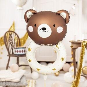 Op de afbeelding: Een bruine beer-vormige ballon met een witte ring versierd met gouden sterren. De ballon heeft een schattig gezicht en maakt deel uit van een babyshower-thema, met het woord "BABY" op de achtergrond.