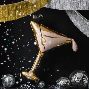 May include: A gold and pink foil balloon shaped like a martini glass with confetti falling around it. There are silver disco balls in the background.