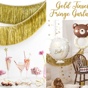 Pu&ograve; includere: Ghirlanda di frange dorate con paillettes con un palloncino bianco che dice "Oh Baby" e un palloncino a forma di orso marrone con un anello. La ghirlanda viene anche utilizzata per decorare un tavolo con bevande rosa e un piatto di caramelle al cioccolato.