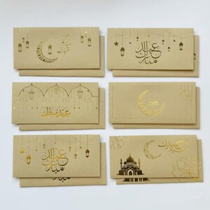 May include: A collection of six beige greeting card envelopes with gold foil designs. The designs include crescent moons, lanterns, stars, and Arabic calligraphy. The envelopes are arranged in two rows of three.