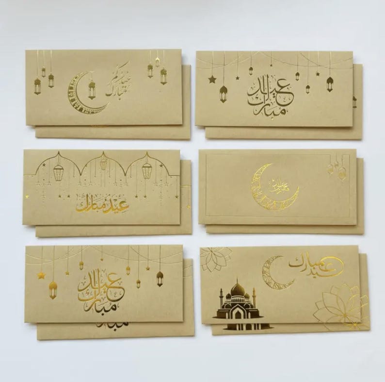 May include: A collection of six beige greeting card envelopes with gold foil designs. The designs include crescent moons, lanterns, stars, and Arabic calligraphy. The envelopes are arranged in two rows of three.