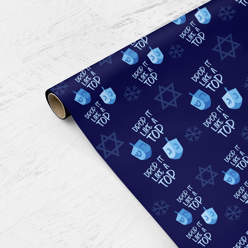 May include: Blue wrapping paper with a repeating pattern of blue dreidels, white snowflakes, and gold six-pointed stars. The text "Drop it like a top" is repeated throughout the pattern.