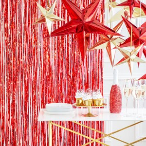 Op de afbeelding: Een tafelsetting met rode en gouden folie sterdecoraties, champagneflutes, een fles mousserende wijn en cupcakes. De tafel is gedekt op een rode folie achtergrond.