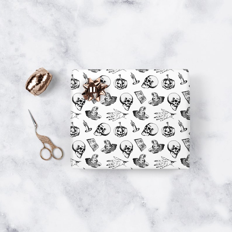 May include: White wrapping paper with a black and white Halloween pattern. The pattern includes skulls, pumpkins, witches' hats, and candles. The wrapping paper is shown with a gold ribbon bow on top.