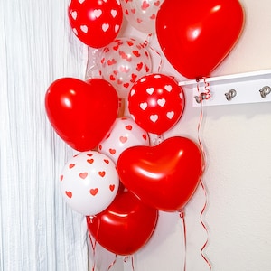 May include: A cluster of red and white heart-shaped balloons with white polka dots. The balloons are tied together with red ribbon and are hanging from a white wall.