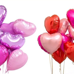 May include: A bouquet of heart-shaped balloons in shades of pink, purple, and red. The balloons are tied together with ribbons and are floating in the air.